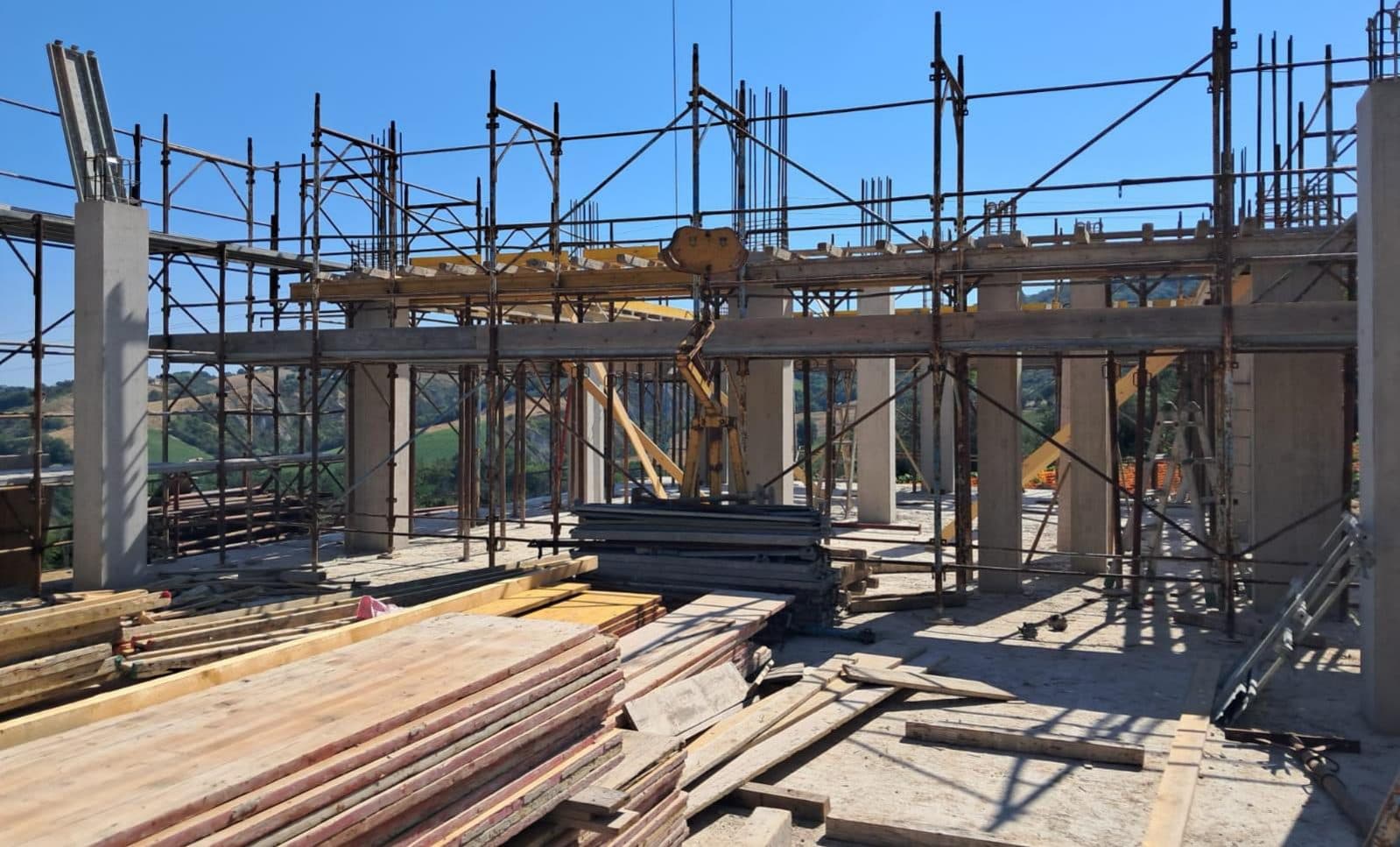 La struttura portante al primo piano coi ponteggi montati e il legname da carpenteria accatastato in cantiere.