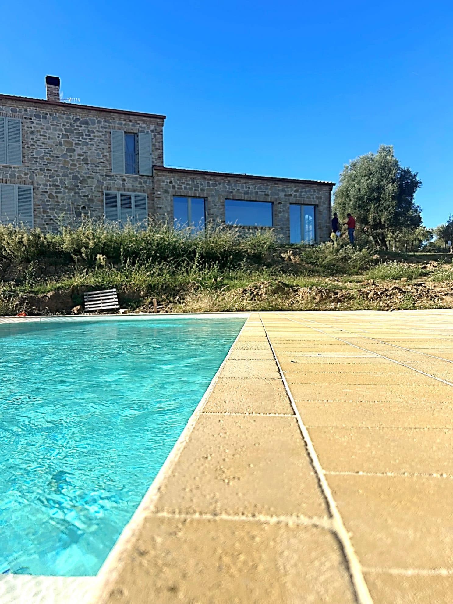 Il costruito finito: la piscina in primo piano e la casa in pietra dietro, con gli olivi sul pendio.
